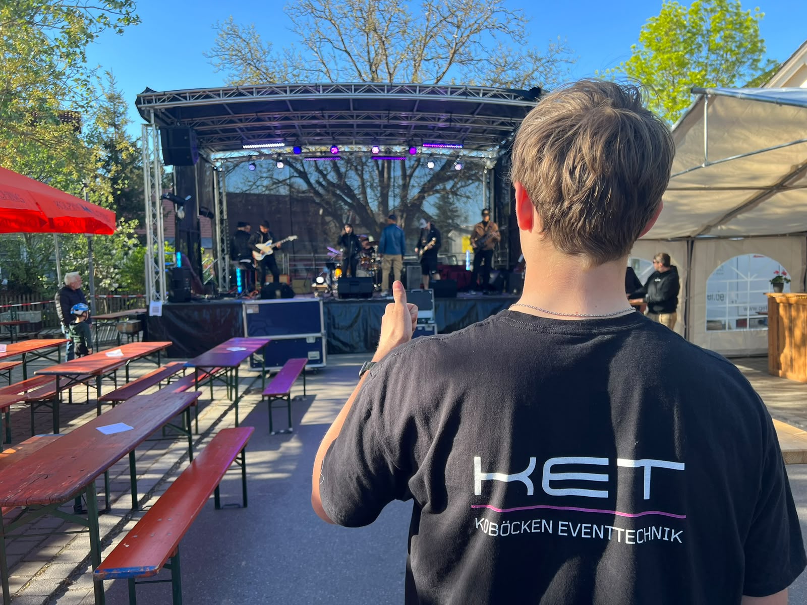 KET-Mitarbeiter im Firmen-T-Shirt gibt vor der Bühne mit Truss-Rig und Band Daumen hoch bei Tanz in den Mai in Olching